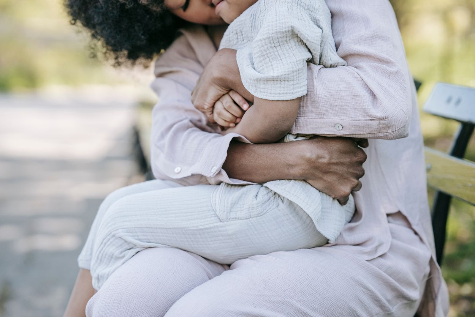 A parent holds their young child close on a park bench in soft, warm light — the calm, everyday tenderness Parent Starts is built around.
